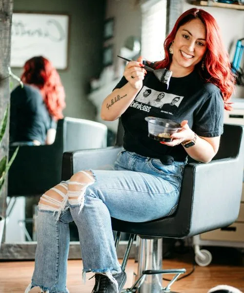 Sara in a styling chair with a color brush and a bowl of color