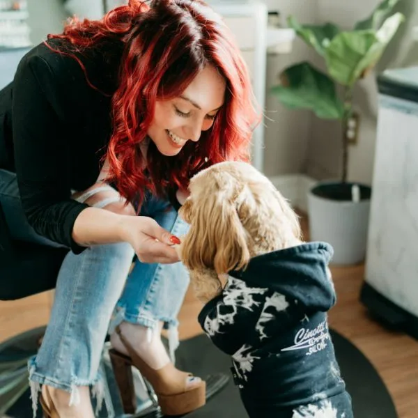 Sara crouching to greet Chloe, the salon's cockapoo, in a Cinotti's Salon hoodie